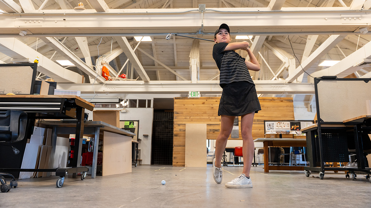Woman swinging a golf club in an architecture classroom.